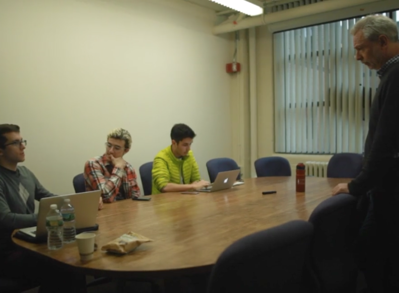 Faculty member standing in office with students at table