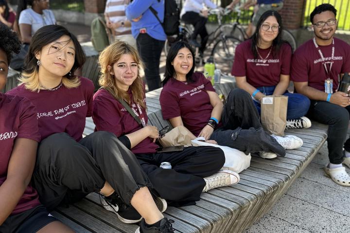 5 students taking a break during global day of service. they are sitting in science center plaza. all of them are wearing crimson shirts that say "global day of service"