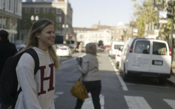 Student wearing Harvard sweatshirt walking towards Harvard Yard