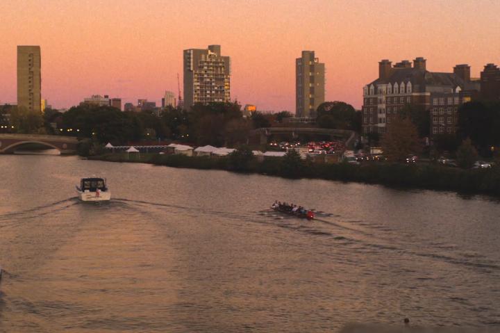 A series of boats rows down the Charles River at dawn.
